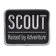 Rektangulärt märke med grå langetterad kant och svart bakgrund med texten SCOUT Raised by Adventure på