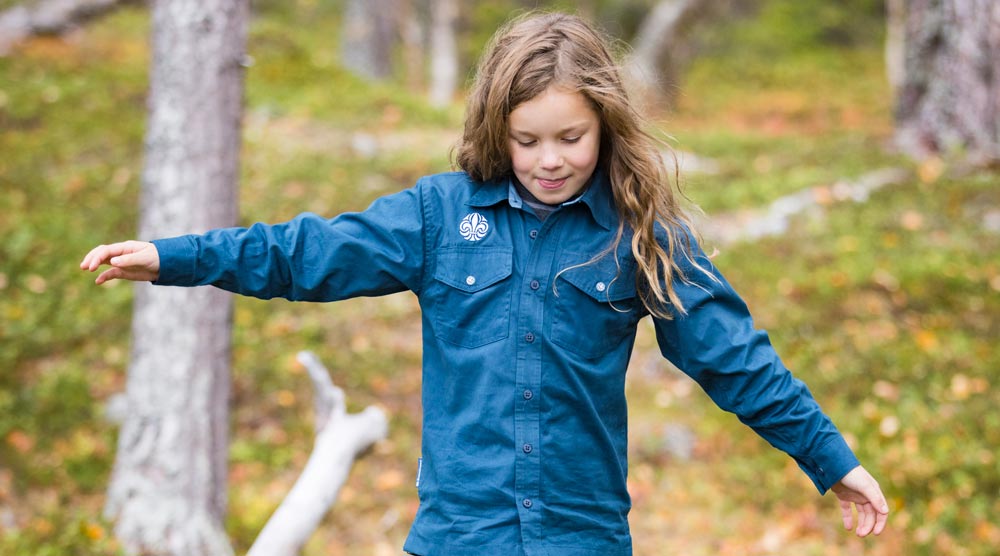 Ett barn med scoutskjorta balanserar på en stock